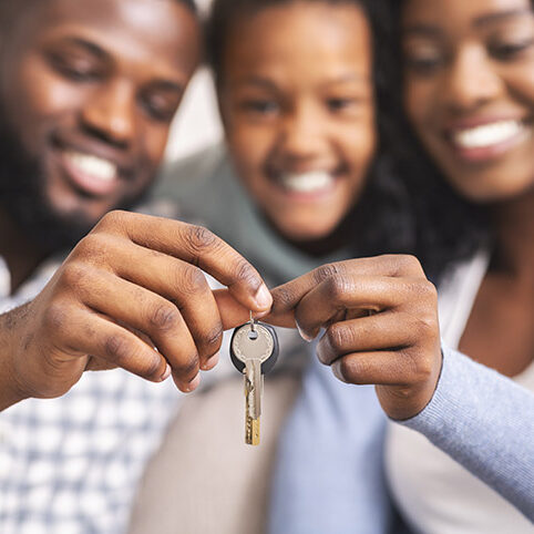 Housing concept. Happy black family with daughter holding keys from their new home, selective focus on hands, closeup.